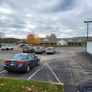 A view of a mostly empty parking lot with a mix of vehicles under a cloudy sky, surrounded by autumn foliage.