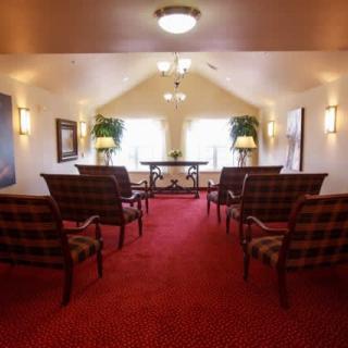 A small chapel with chairs arranged in rows, featuring red carpet and soft lighting.