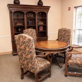 A dining area with a round wooden table, upholstered chairs, and a bookshelf.