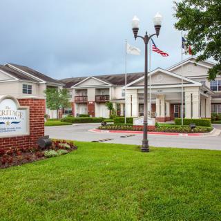 An exterior view of a building with a neatly manicured lawn, sign, and flags at the entrance.