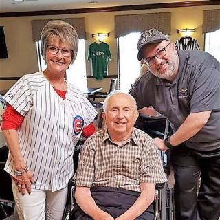 A cheerful group of three people, including an elderly individual in a wheelchair, posing indoors.
