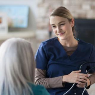 A nurse in a navy blue uniform talks with an elderly woman.
