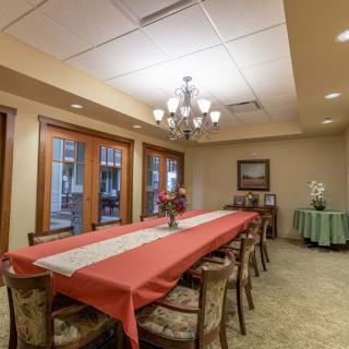 A well-decorated dining room with a long table and chairs, featuring a chandelier and floral centerpieces.