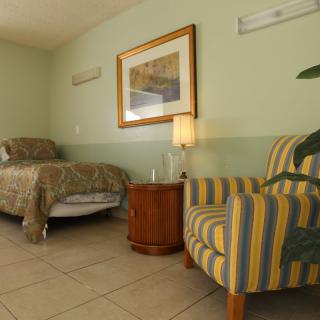 A cozy bedroom with a single bed, striped armchair, and nightstand with a lamp.