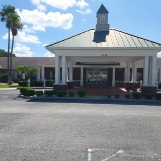 A building entrance with a driveway lined by palm trees under a sunny sky.