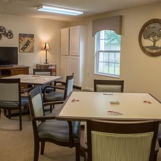 A cozy interior living area with tables and chairs, decorated with artwork and a window providing natural light.