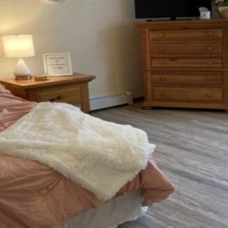 A cozy bedroom with a bed, nightstand, lamp, and dresser.