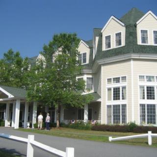 A large building with multiple windows and a green roof, surrounded by trees on a sunny day.