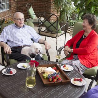 A group of people enjoying food and conversation on a patio with a small dog sitting on one person's lap.