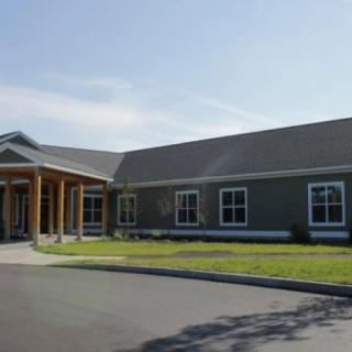 A single-story commercial building with a covered entrance and several windows, set against a clear blue sky.