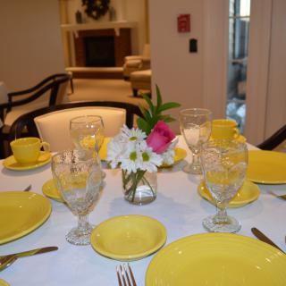 A beautifully set dining table with yellow dishes and a floral centerpiece.