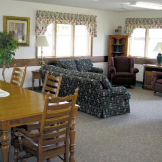 A cozy living room with a sofa, armchairs, and a dining table near large windows.