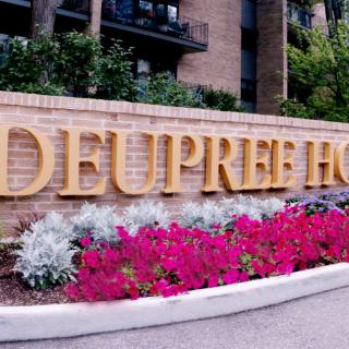 A brick wall with golden lettering and vibrant flowers in front of a building.