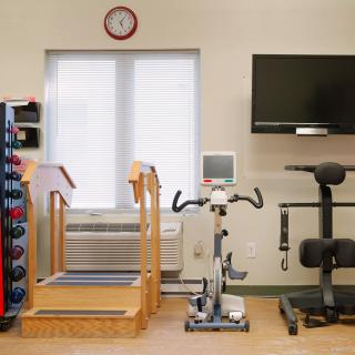 A rehabilitation gym with various exercise equipment including a treadmill, stationary bike, and weights, along with a mounted television.