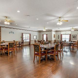 A spacious dining room featuring multiple tables and chairs, with wooden flooring and ceiling fans.