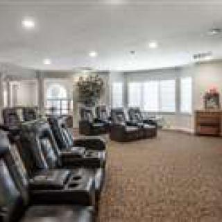 A cozy theater room with several recliners arranged in rows, featuring large windows and a carpeted floor.