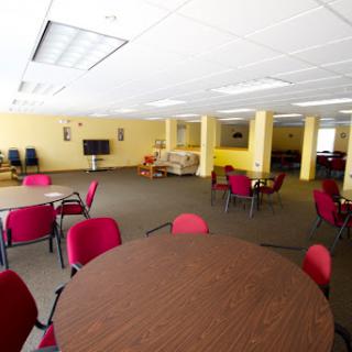 A spacious meeting room featuring round tables and red chairs, designed for community gatherings.