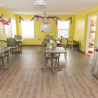 A cheerful dining area with yellow walls, furnished with tables and chairs, perfect for communal gatherings.