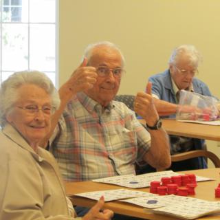 A group of senior citizens enjoying a game of bingo, with one giving a thumbs up gesture.