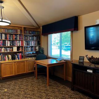 A cozy library corner with bookshelves, a table by the window, and a television on the wall.