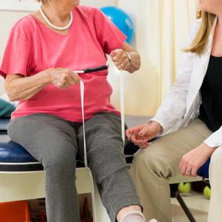 A therapist assists an elderly woman with a physical therapy exercise.