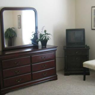 A bedroom with a dresser and mirror next to a vintage television.