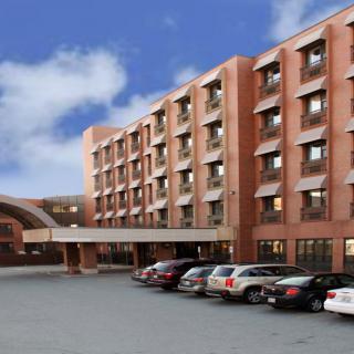 A large brick hotel building with multiple floors and a parking lot filled with cars.