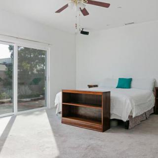 A minimalist bedroom with a bed, ceiling fan, and plenty of natural light from a large window.