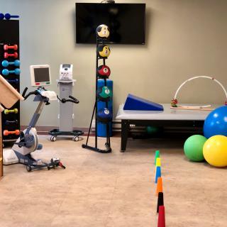A physical therapy room equipped with exercise and rehabilitation tools, including fitness balls and an exercise bike.