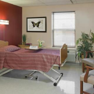 A well-furnished hospital room featuring a patient bed, a window with blinds, and wall decorations.