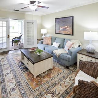 A cozy and well-decorated living room with a blue sofa, patterned rug, and wooden coffee table.