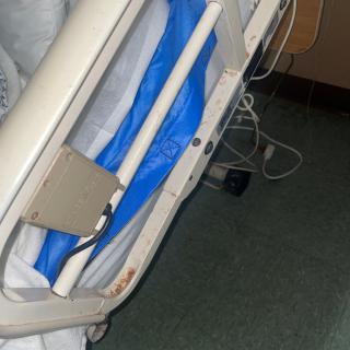 A hospital bed with side rails, featuring a blue sheet and medical equipment nearby.
