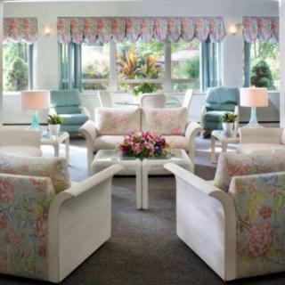 A cozy living room with floral-patterned armchairs and a central coffee table, accentuated by natural light from large windows.