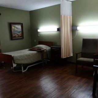A hospital room with a single bed, artwork on the wall, and basic furniture.