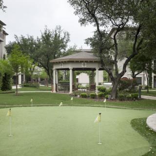 A scenic garden with a gazebo and putting green, surrounded by trees.