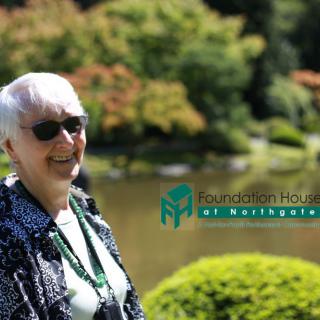 An elderly woman wearing sunglasses enjoys a sunny day in a lush garden.