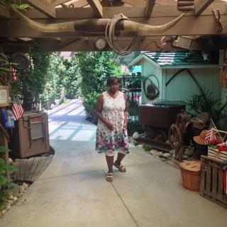 A woman in a summer dress walks down a shaded garden pathway surrounded by greenery.