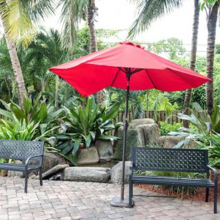 A serene patio area with a red umbrella and benches surrounded by lush tropical plants.