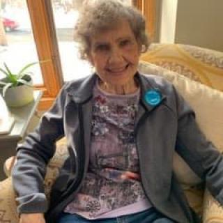 An elderly woman smiling while seated comfortably indoors.