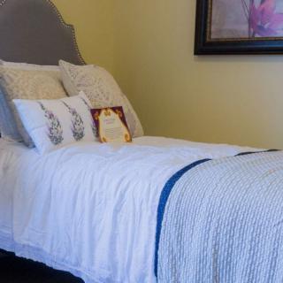 A neatly made bed in a cozy bedroom with decorative pillows and a painting on the wall.