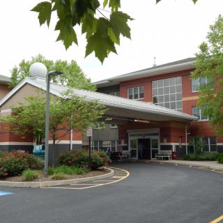 Entrance of a brick hospital building surrounded by trees.