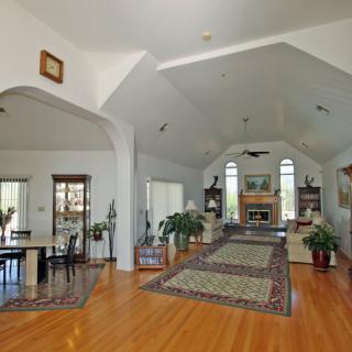 A spacious living room with vaulted ceilings, hardwood floors, and a cozy fireplace surrounded by large windows.