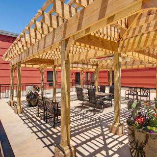 A sunlit patio features a wooden pergola with outdoor seating arrangements.