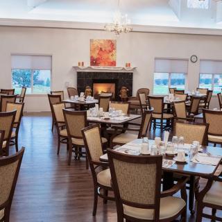 A well-lit dining room with neatly arranged tables and chairs, featuring a central fireplace.