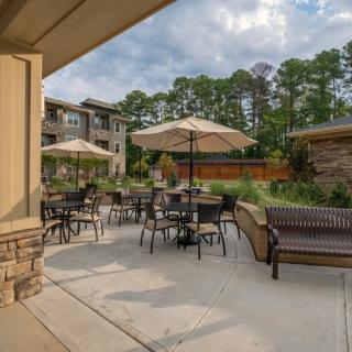 A peaceful outdoor patio with tables, chairs, and umbrellas set amidst an apartment complex with lush greenery.