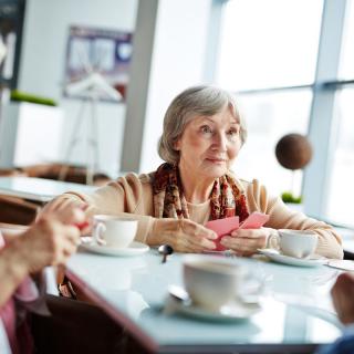 An elderly woman enjoying tea and conversation in a cafe.