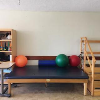A physical therapy room with a treatment table, gym balls, and stairs for rehabilitation exercises.