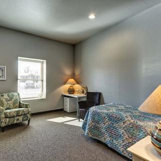 A cozy bedroom with a single bed, desk, and armchair next to a window.