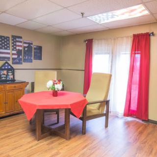 A cozy room featuring a round table with red cloth, two comfortable chairs, and vibrant curtains.
