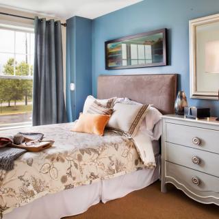 A cozy bedroom with blue walls, a well-decorated bed, and a stylish nightstand.